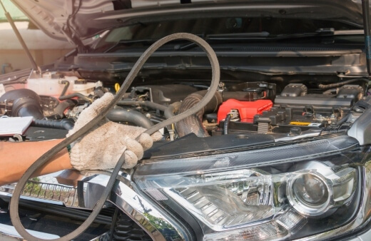 A mechanic wearing gloves replaces a worn-out drive belt in a car engine bay during a car belt replacement in Sydney by True Blue Mobile Mechanics. A mechanic wearing gloves replaces a worn-out drive belt in a car engine bay during a car belt replacement in Sydney by True Blue Mobile Mechanics.